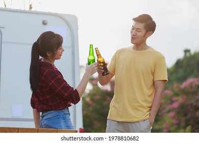Travel Asian couple having fun drinking beers standing in front of vintage camper mini van. Happy people enjoying drink and camping by the nature. Concept of leisure vacation lifestyle. - Powered by Shutterstock