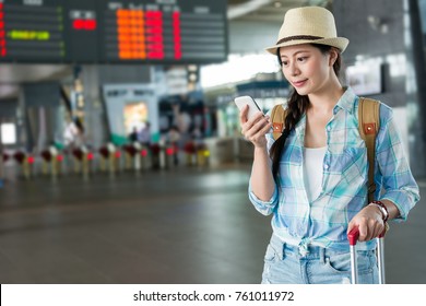 Travel Asian woman holding mobile phone reading text message in the Taiwan high speed rail station hall waiting for the train coming.