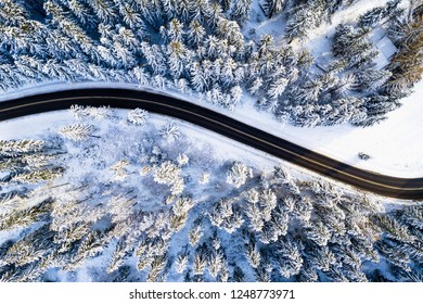 Travel background. Black road in white forest covered with snow. Aerial drone view. Mountain road. Winter landscape with highway.