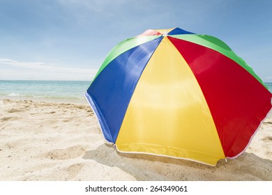 travel background with a colorful sunshade lying in the white sand of a beach with a turquoise sea and a blue sky