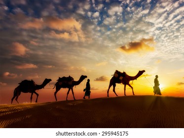 Travel background - two cameleers (camel drivers) with camels silhouettes in dunes of desert on sunset