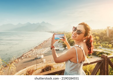 Travel blogger girl takes high-quality and vivid photos on the camera of his new expensive smartphone of the famous Konyaalti beach from a scenic viewpoint in Antalya, Turkey - Shutterstock ID 2190184551