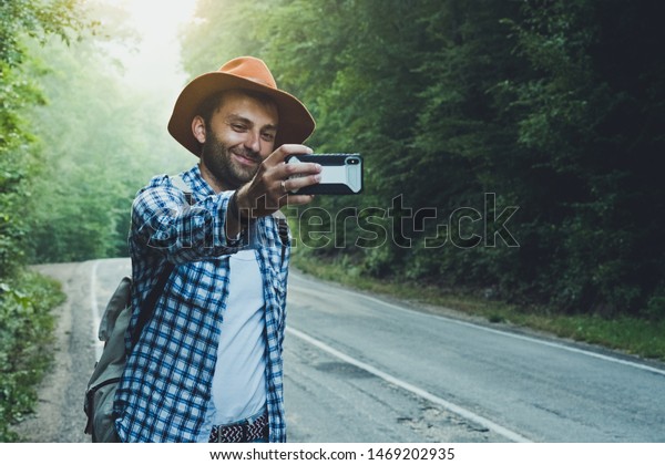 Travel\
blogger man taking a photo or selfie on the background of a foggy\
automobile road. Writes a blog on a\
smartphone.