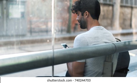 Travel Blogger Watching The Video On A Display Of A Mobile Phone Connected To The Public Wi-fi At The Bus Stop. Bearded Hipster Guy Surfing The Web On A Smartphone While Waiting For The Transport.