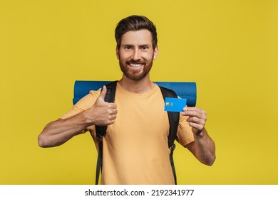 Travel Budget Concept. Happy Middle Aged Man With Tourist Equipment Holding Credit Card And Showing Thumb Up Over Yellow Studio Background. Traveller Planning Funds For His Camping Adventure