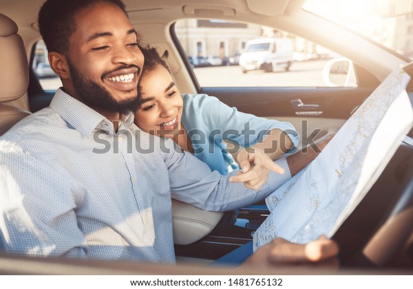 Travel by auto. Happy afro couple with map\
in car, planning their route for\
vacation