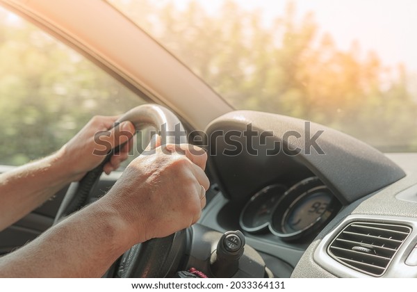 Travel by car at dawn. Hands of\
male driver on steering wheel of car. Sunlight in\
windshield