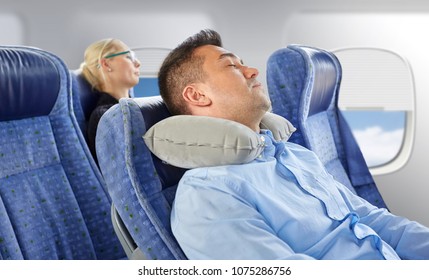 Travel, Comfort And People Concept - Man Sleeping In Plane With Inflatable Cervical Neck Pillow Over Porthole Background