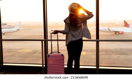Travel concept with back view young tourist woman  holding the luggage and looking the airplane in the hall room with sunlight at the airport - Shutterstock ID 2116068698