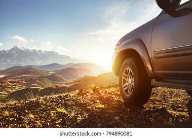 Travel concept with big 4x4 car against sunset and mountains. Closeup photo of offroad wheel