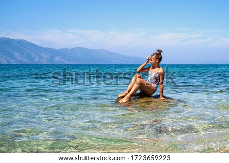 Travel Concept. Clean sea and wild seascape.Young brunette girl enjoying vacation. woman relaxing on coast admiring beautiful seascape. Side view.Girl sitting on a cliff face over the sea.