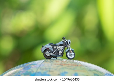Travel Concept. Close up of miniature motorcycle toy on wolrd balloon map with green nature background.