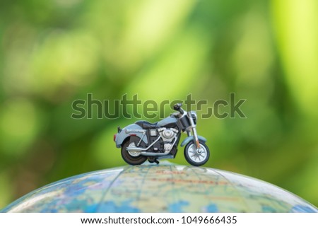 Travel Concept. Close up of miniature motorcycle toy on wolrd balloon map with green nature background.