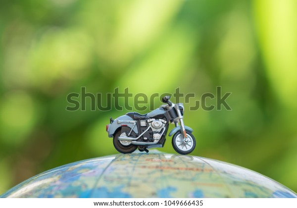 Travel Concept. Close up of\
miniature motorcycle toy on wolrd balloon map with green nature\
background.