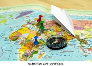 Travel Concept Compass And Paper Airplane On The World Map, The Buttons Mark The Places Of Travel. High Quality Photo