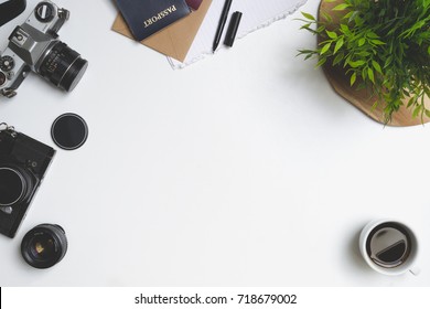 Travel concept. Desk or table filled with (office) supplies. Old vintage camera, envelope, notebook, pen, plant, coffee, passport, phone and lens. View from above. - Shutterstock ID 718679002
