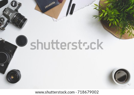 Travel concept. Desk or table filled with (office) supplies. Old vintage camera, envelope, notebook, pen, plant, coffee, passport, phone and lens. View from above.