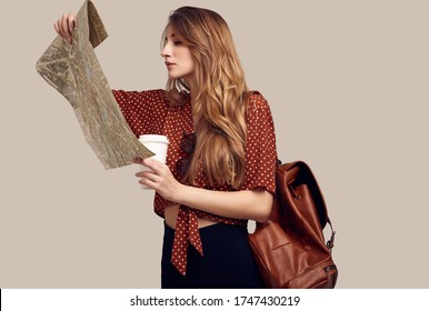 Travel Concept. Dreaming About Journey. Studio Portrait Of Pretty Young Hipster Woman With Backpack Holding Map. Isolated On Gray Background