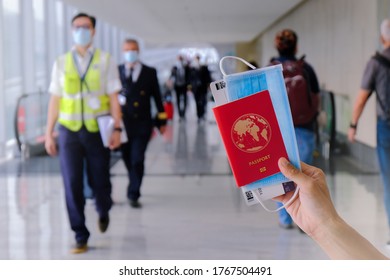 Travel Concept: Hand Holding Passport (GENERIC World Passport) Mask, Boarding Pass. Airport Staff, Pilot  Walking In Background Wearing Face Masks. Reopening; Coronavirus Covid-19; Travel Restrictions