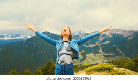 Travel concept, happy woman enjoying fresh air mountains raising her hands up on Andorra mountain background