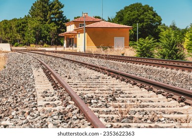 travel concept image with train tracks in the foreground and an empty train station out of focus in the background - Powered by Shutterstock