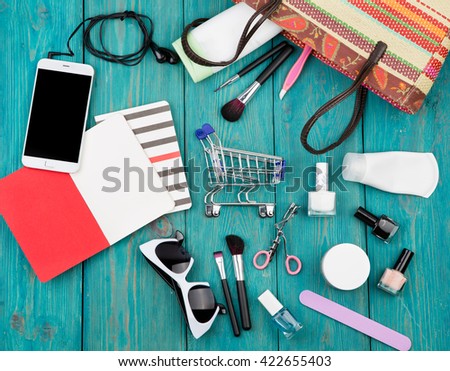 Travel concept - summer women set with straw bag, smartphone with headphones, notepads, sunglasses, shopping carts, cosmetics makeup and essentials on blue wooden background