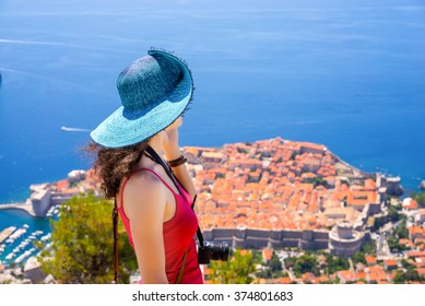 Travel Concept. Top View Of Young Woman-traveler With Camera Looking On Adriatic Sea And Dubrovnik - Old Beautiful Medieval City In Croatia, Europe. Blurred Background With Copy Space Area For A Text