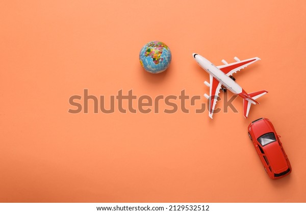 Travel concept. Toy\
model of car and airplane, globe on coral-colored background. Top\
view. Copy space