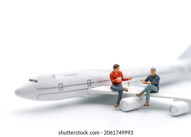 Travel Concept. Two Man Miniature Figure People With Cup Of Coffee Sitting And Talking On Wing Of Airplane Toy Model On White Background.