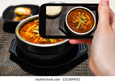 travel concept - visitor photographs of korean cuisine of yukgaejang (spicy soup with beef, eggs, mushrooms, starch noodles, scallions, ferns, bean sprouts, served with boiled rice) on smartphone - Powered by Shutterstock