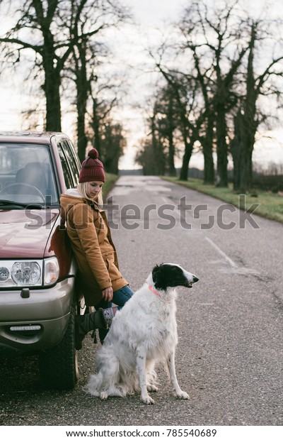 Travel with dog. Woman traveling\
with her dog. Standing by off road vehicle on the road.\
