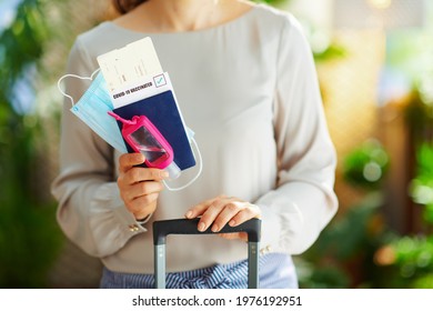 Travel During Coronavirus Pandemic. Closeup On 40 Years Old Woman With An Antibacterial Agent, Trolley Bag, Air Tickets, Medical Mask And Covid Passport At Modern Home In Sunny Day.