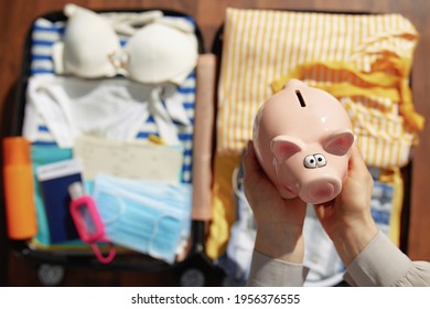 Travel During Coronavirus Pandemic. Upper View Of Modern Female With An Antibacterial Agent, Trolley Bag, Medical Mask And Piggy Bank In The Modern House In Sunny Day.