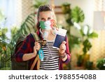 Travel during covid-19 pandemic. Portrait of happy hipster solo traveller woman with covid passport, italian flag medical mask, backpack and antiseptic at modern home in sunny day.