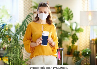 Travel During Covid-19 Pandemic. Young Woman With Covid Passport, Medical Mask, Air Ticket, Trolley Bag, An Antibacterial Agent And Sunglasses In The Modern House In Sunny Day.