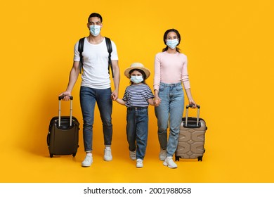 Travel During Pandemic. Arab Tourists Family Wearing Protective Masks Walking With Suitcases Over Yellow Background In Studio, Middle Eastern Parents And Child Going To Airport, Copy Space