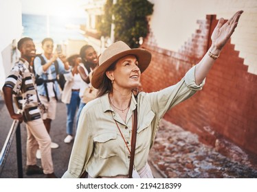Travel, education and a teacher with students on school field trip, on urban tour. Woman, city guide and group of happy tourists, pointing at local architecture and learning on international holiday - Shutterstock ID 2194218399