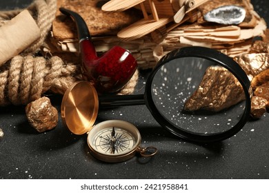 Travel equipment with smoking pipe, magnifier and golden nuggets on grunge black background