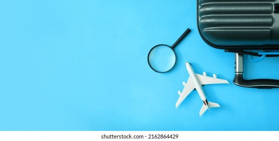 Travel Flat Lay Composition Of Suitcase With Airplane, Magnifier On Blue Background. Prepare Trip Concept. Banner.