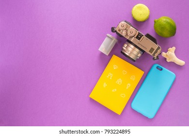 Travel Flat Lay With Vintage Camera, Lime, Film Roll, Passport, Iphone Case, Sea Coral And Green Macaroon On Purple Background
