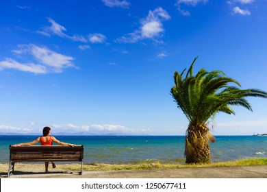 Travel Freedom Concept. Tourist Mature Woman Sitting On Bench On Sea Shore Enjoying Summer Vacation, Looking At Ocean