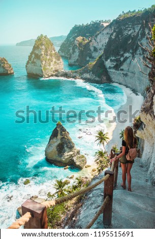 A travel girl with backpack and in shorts on the ocean, cliffs and tropical beach background. Nusa Penida, Indonesia. Female silhouette