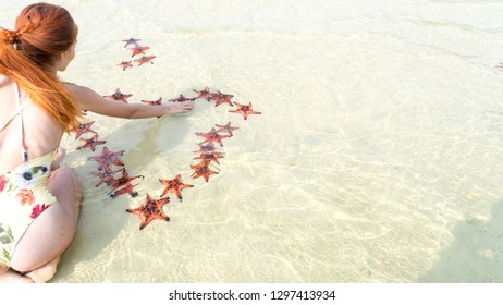 Travel girl in bikini with starfishes,making a heart for Valentines Day in honeymoon in Phu Quoc island with clear water and white sand beach