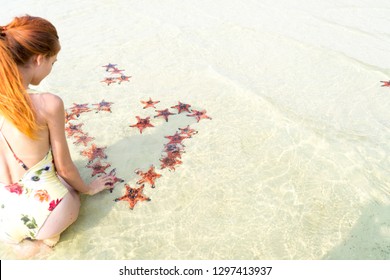 Travel girl in bikini with starfishes,making a heart for Valentines Day in honeymoon in Phu Quoc island with clear water and white sand beach