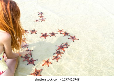 Travel girl in bikini with starfishes,making a heart for Valentines Day in honeymoon in Phu Quoc island with clear water and white sand beach