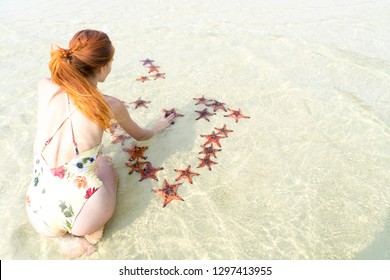 Travel girl in bikini with starfishes,making a heart for Valentines Day in honeymoon in Phu Quoc island with clear water and white sand beach