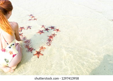 Travel girl in bikini with starfishes,making a heart for Valentines Day in honeymoon in Phu Quoc island with clear water and white sand beach