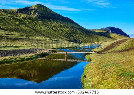 Travel to Iceland. Beautiful Icelandic landscape with bridge over creek, mountains, sky and clouds. Trekking in national park Landmannalaugar
