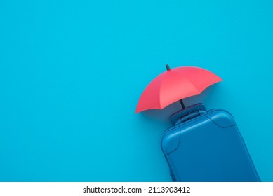 Travel insurance business concept. Red umbrella cover suitcases travelers on blue background copy space. Travel insurance covers loss suitcase, flight delays, cancellations, accident, medical expenses