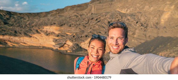 Travel interracial couple tourists traveling in Spain taking selfie photo on hike. Banner panoramic of Asian woman, caucasian man hikers happy. - Powered by Shutterstock